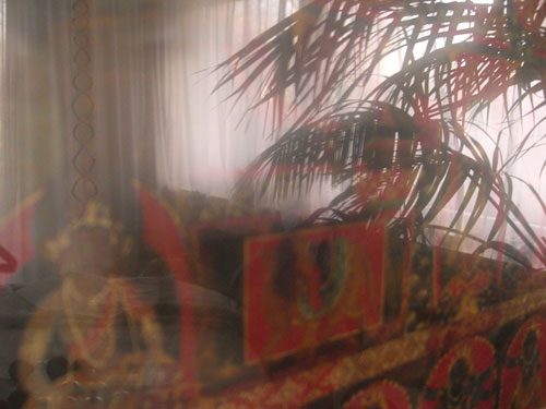 Bild eines tibetischen Tangka mit einer yogischen Sitzhaltung, mit Spiegelung von Fenster & Palmblättern